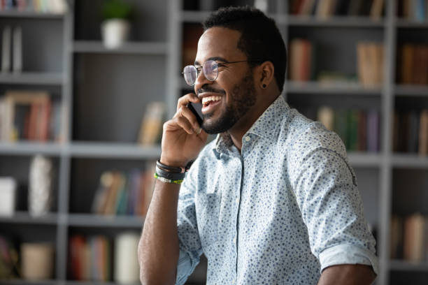 empresario africano sosteniendo teléfono móvil disfrutan de conversación informal - person on phone fotografías e imágenes de stock