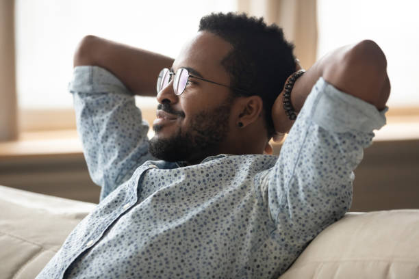 istock Calm African guy puts hands behind head relaxing on couch 1253877753