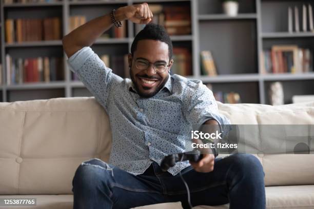 Excited African Guy Holding Joypad Celebrating Victory In Playstation Games Stock Photo - Download Image Now