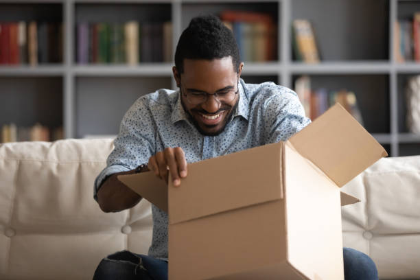 istock African guy opening parcel box seated on couch at home 1253877784