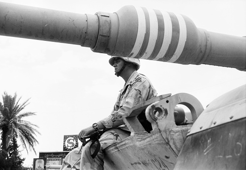 An American soldier sits with his rifle on a US tank and observes the surroundings. US Army soldiers surveillance base in Baghdad / Iraq during the Gulf War between the USA and Iraq. Photographed by Michael Multhoff in Baghdad / Iraq. May 12, 2003