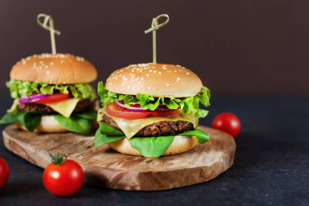 istock Beef burger with fresh salad, cheese and tomatoes on dark background. 1253882825