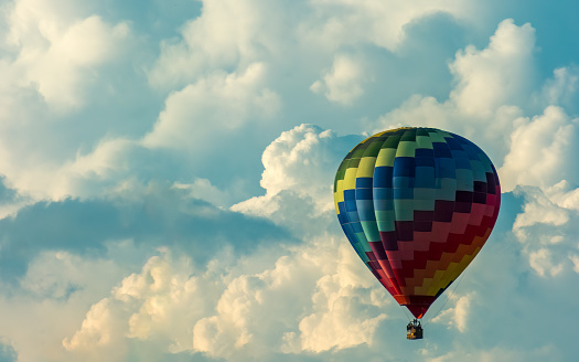 Colorful hot air balloon drifting slowly over cumulonimbus clouds formation.