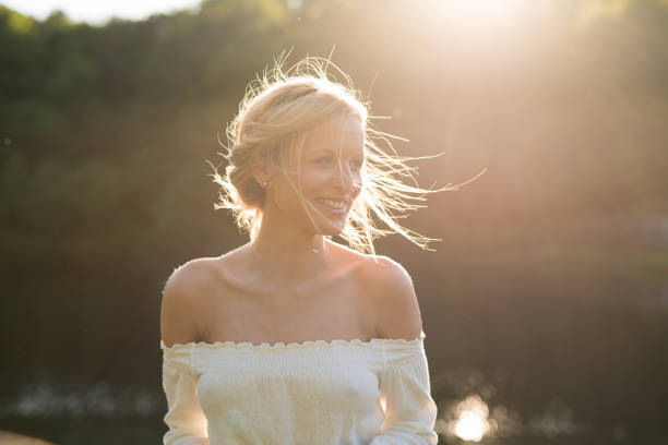 Happy young blonde woman. She is wearing a white shirt and has long hair tied. She looks to the left and laughs.