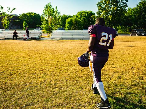 African American Junior Football player getting during game practice at the outdoor field. He is walking off the field.
