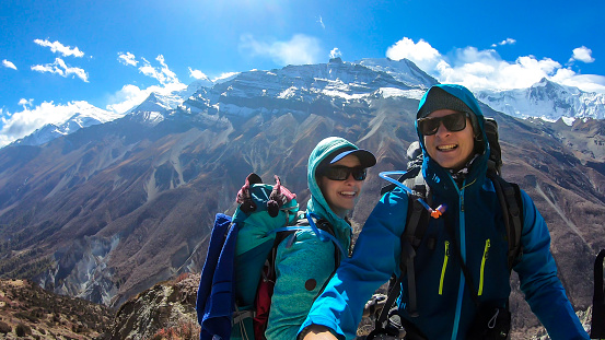 A couple taking a selfie while trekking Annapurna Circus in Himalayas, Nepal, with the view on Annapurna Chain. Dry and desolated landscape. High, snow capped mountain peaks. Happiness and love