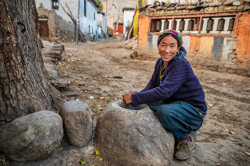 Tibetan woman using a stone mortar to make flour, small village in Upper Mustang. Mustang region is the former Kingdom of Lo and now part of Nepal,  in the north-central part of that country, bordering the People's Republic of China on the Tibetan plateau between the Nepalese provinces of Dolpo and Manang.