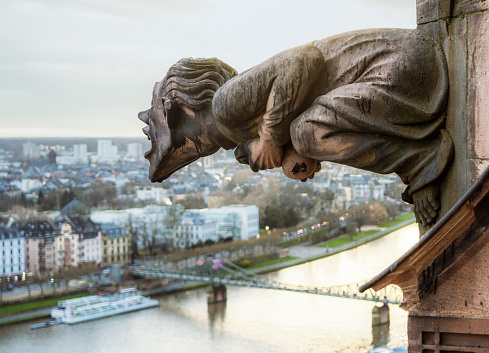 A medieval gargoyle, part of the exterior stonework of Frankfurt Cathedral's spire, appearing to shout over the city.\n\nThe cathedral, including the gargoyles and other exterior features, was completed in its present form during the mid-16th Century. Following that, restorative work was undertaken in 1867 after a fire.