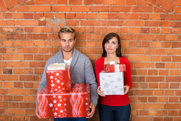 Frowning Lovers Holding Christmas Gifts Frowning Young Lovers Holding Christmas Gift Boxes. Leaning on Bricks Wall. derogatory stock pictures, royalty-free photos & images
