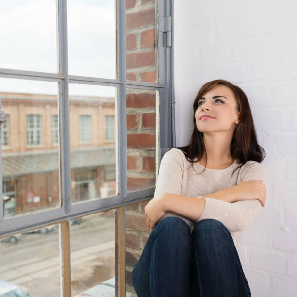 istock Young woman sitting daydreaming on a windowsill 1253895624