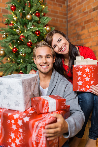 Close up Happy Young Sweet Couple with Assorted Size Gift Boxes in Front the Attractive Christmas Tree.