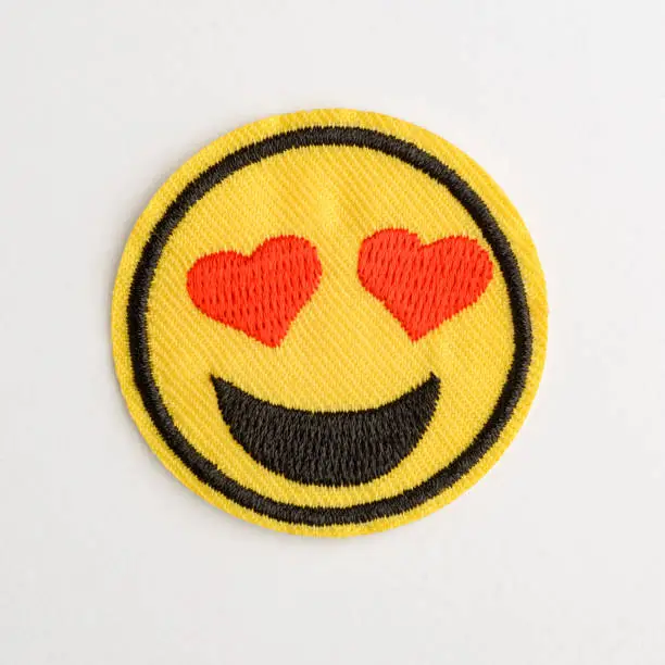 Lovey dovey emoji patch on white background. Funny and romantic, embroidered decorative element to style up your wear.