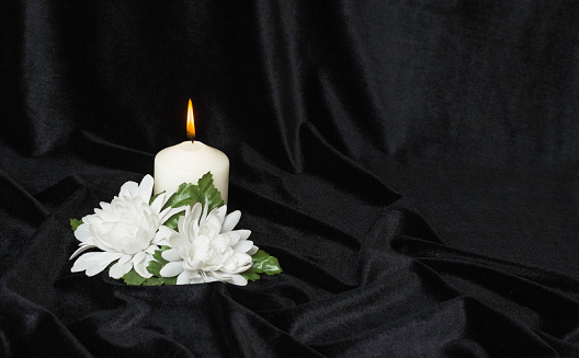 Condolence card. White burning candle and white flowers on a black background, free space for text.