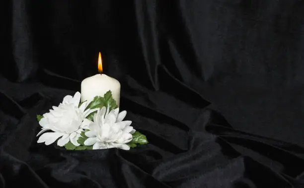 Photo of Condolence card. White burning candle and white flowers on a black background, free space for text.