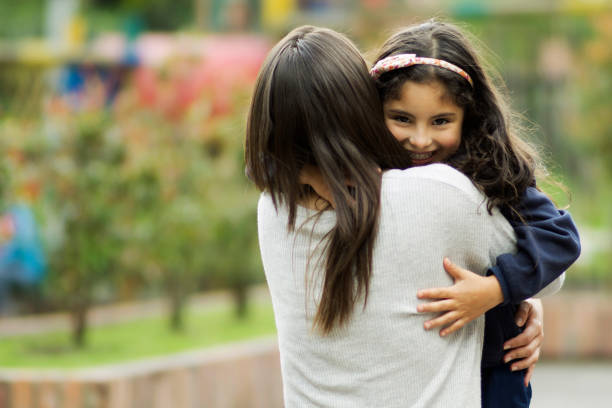 istock Cheerful little girl smiling at camera while hugging mommy 1253914040