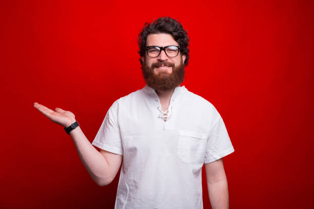 istock Smiling man is presenting something with his hand over red background. 1253914215