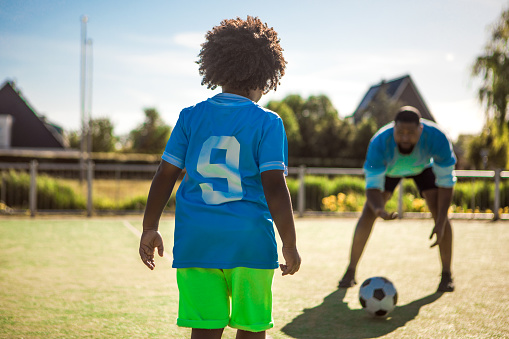 An african american father and young son playing soccer on a neighbourhood football pitch on a beautiful sunny day in the Netherlands