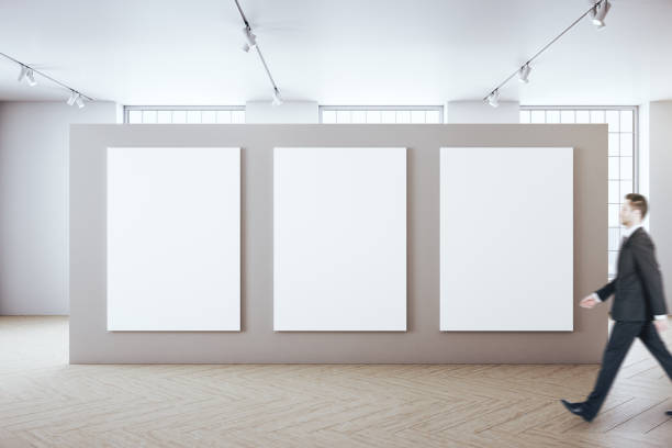 istock Businessman walking in modern hall interior with three blank poster 1253918671