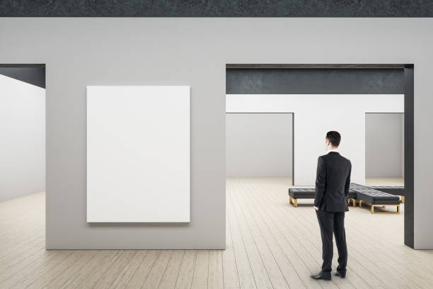 istock Businessman looking on blank billboard in minimalistic gallery interior. 1253923131