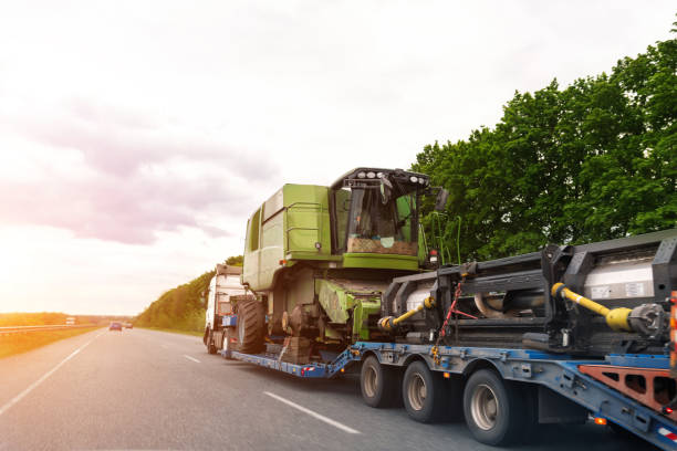 camión industrial pesado con transporte de plataforma semirremolque desmontado máquina cosechadora combinada en la carretera común en la carretera del atardecer o el día del amanecer. servicio de transporte de equipos agrícolas - personal transportation fotografías e imágenes de stock