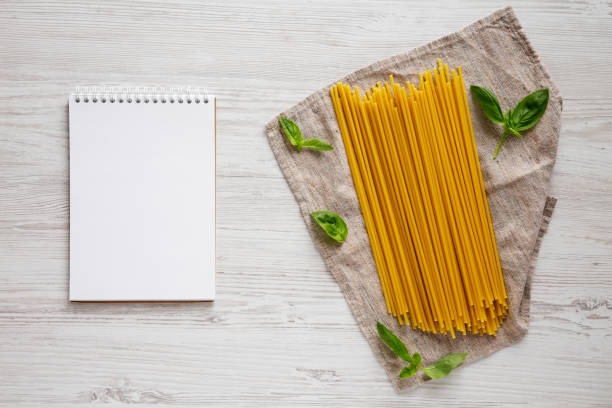 istock Uncooked Dry Organic Bucatini Pasta, blank notepad on a white wooden surface, top view. From above, flat lay, overhead. Copy space. 1253929590