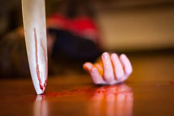 Photo of Close up on a bloody knife planted on a wooden floor, a killing scene