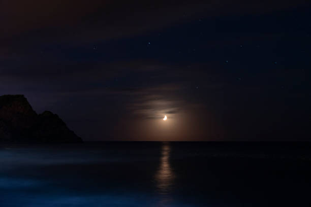 moon in clouds over sea in night and stars.