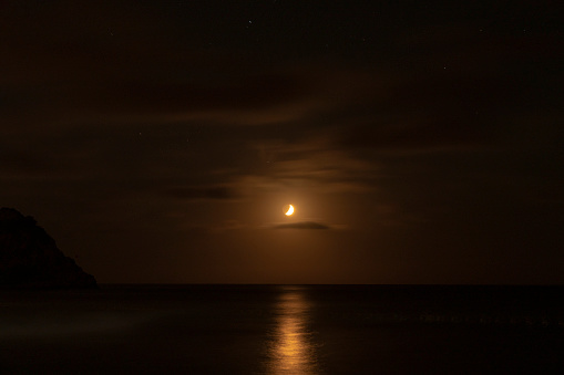 moon in clouds over sea in night and stars.