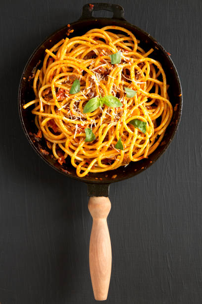 Tasty Homemade Bucatini all Amatriciana Pasta in a cast iron pan on a black background, top view. Flat lay, overhead. Tasty Homemade Bucatini all Amatriciana Pasta in a cast iron pan on a black background, top view. Flat lay, overhead. all'amatriciana stock pictures, royalty-free photos & images