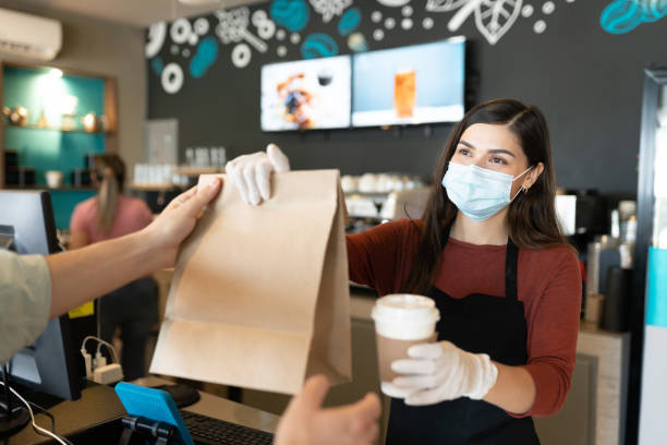 Female Barista Giving Parcel And Coffee To Customer Young female staff giving parcel and coffee to customer at takeaway counter in coffee shop serving food and drinks photos stock pictures, royalty-free photos & images