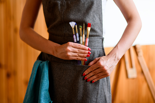 Close-up view of woman in gray apron who holds several paint brushes in her hand