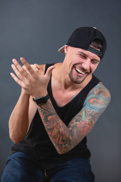 Studio portrait of a young tattooed man sitting in front of a black background wearing a tank top