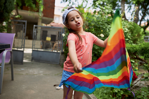 Little preschool aged girl playing with a rainbow colored kite in her home backyard