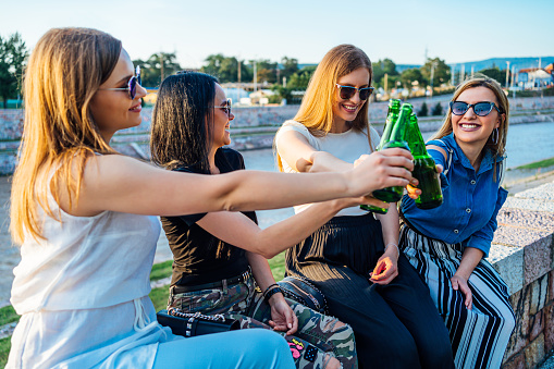 Four happy female friends toasting with beer bottles outdoors