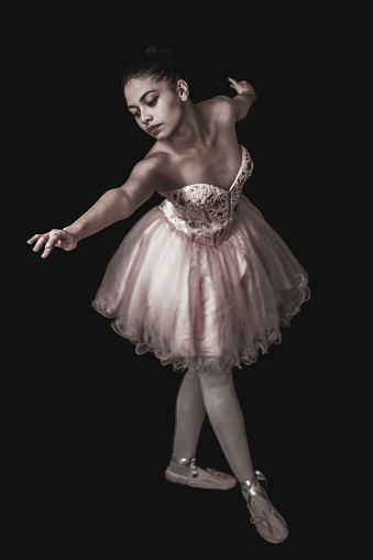 Young latin american ballerina performing over black background