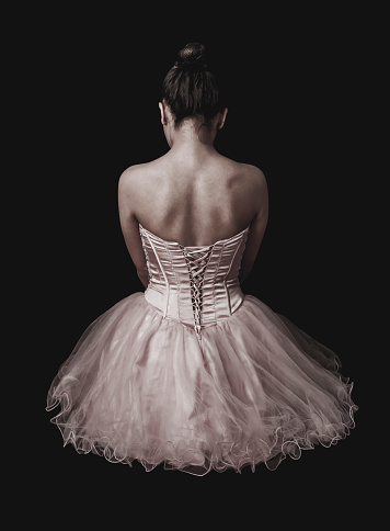 Back view of ballerina sitting on floor wearing her costume over black background