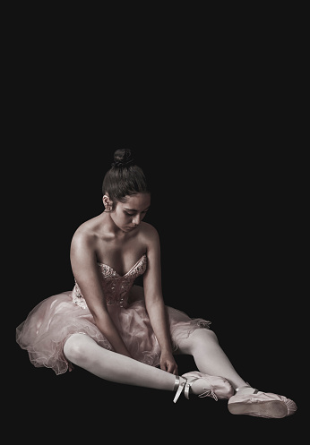 Sad ballerina sitting on floor defeated over black background