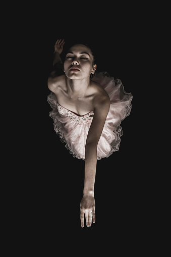 Beautiful ballerina performing with eyes closed on black background