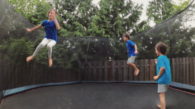 Children jumping on a trampoline in a backyard without parents around