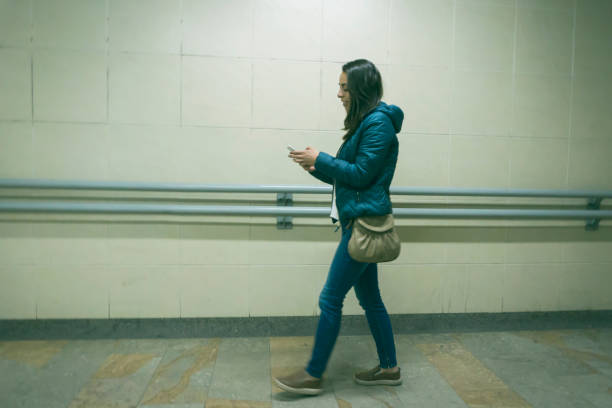Young woman walking at an underground station while texting on smartphone - Lifestyles
