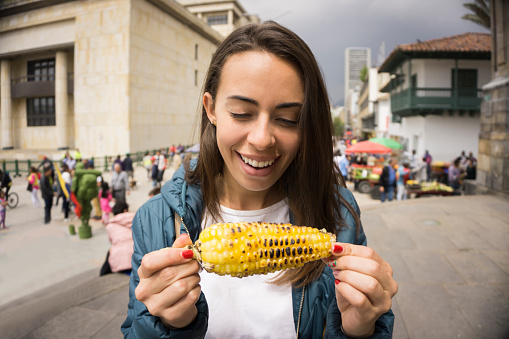 Happy young woman eating a delicious corn on the cob while doing tourism