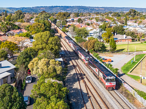Adelaide, Australia - June 27, 2020: Aerial view of Specialised Container Transport (SCT) interstate freight train 6MP9 with 4 powerful diesel locomotives passes through Adelaide Suburbs en route from Melbourne to Perth with a heavy train of supplies for Western Australia. The train is descending after crossing the Adelaide Hills seen in the background.