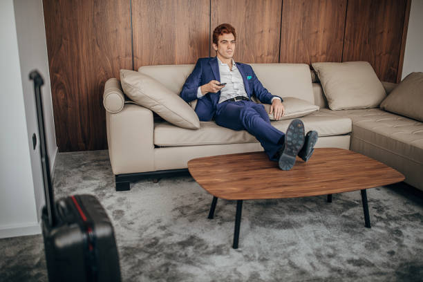 One man, handsome businessman in blue suit in hotel room, changing channels on remote control.