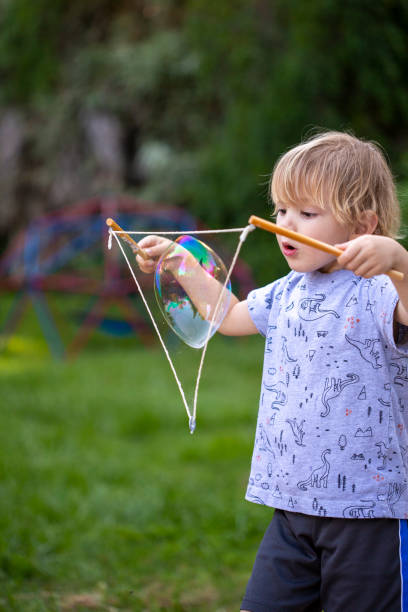istock Young boy, 4 years old, blowing large bubbles with string outside 1253978520