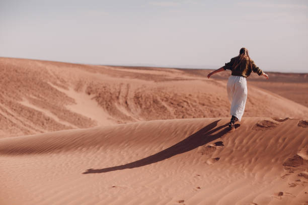istock Young woman runs on sand dunes in desert Sahara 1253980232