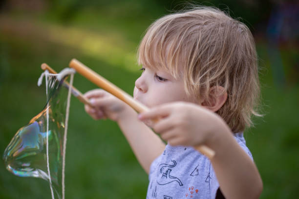 istock Young boy, 4 years old, blowing large bubbles with string outside 1253981254