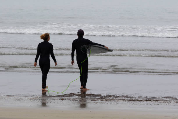 Young multiracial African American lady & a Japanese surf instructor setting up a surfboard