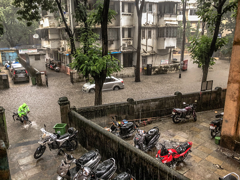 Parel, Mumbai / India - 3rd July 2020 - A man pushes his bicycle into the building as you see the whole street is flooded inder water
