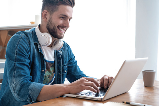 Cheerful blogger. Handsome modern man designer working on laptop online, using internet at home