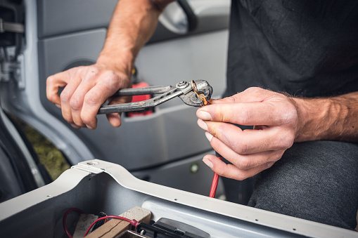 Close-up of hands with a copper cable and pliers. A cable lug is being attached to the cable.